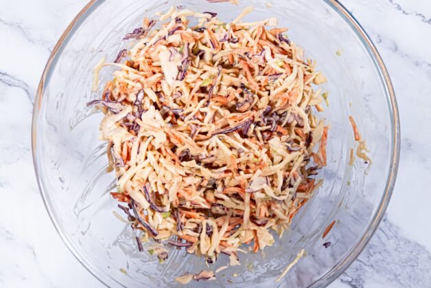 A glass bowl of coleslaw salad after mixing the shredded vegetables with the creamy dressing.