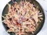 Top-down view of creamy coleslaw salad with shredded green and red cabbage, carrots, and a tangy dressing in a dark bowl.