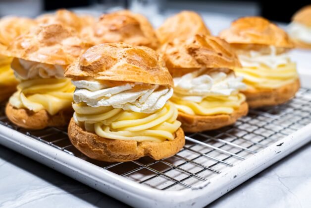 Golden cream puffs filled with silky vanilla pastry cream and fluffy whipped cream, cooling on a wire rack, ready to be enjoyed.