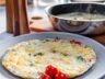 A freshly cooked egg white frittata with melted cheese, spinach, and bell peppers on a plate, with a steaming skillet in the background.