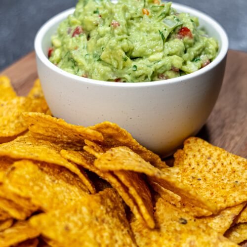 Fresh homemade guacamole with avocado, lime, tomato, and cilantro, served with crispy tortilla chips.