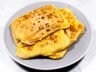 A plate of crispy, golden-brown Roti Prata filled with eggs and cheese, freshly cooked and ready to serve.