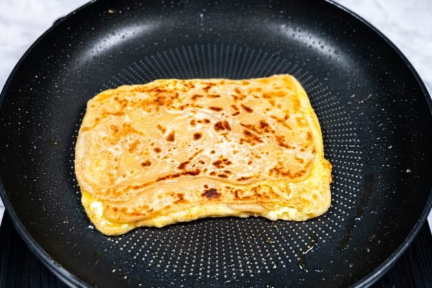 Golden brown Roti Prata cooking in a pan, crispy and flaky.