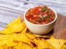 Fresh homemade salsa with tomatoes, jalapeño, red onion, and cilantro, served with crispy tortilla chips on a wooden board.