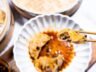 A juicy shrimp & pork dumpling held by chopsticks, dipped in a spicy soy-based sauce.