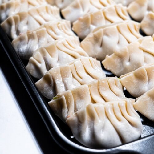 Freshly wrapped shrimp and pork dumplings arranged in a pan, ready to be cooked.