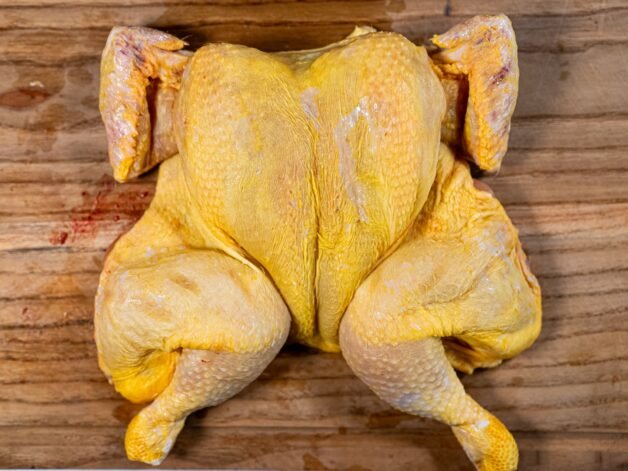 Flattened, fully spatchcocked chicken placed on a wooden cutting board, ready for seasoning.
