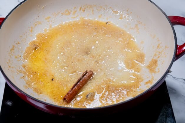 Melted butter with sautéed garlic, ginger, cinnamon, and cardamom in a pan, releasing rich aromas for Butter Chicken.