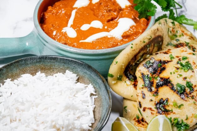 Butter Chicken served with basmati rice, garlic naan, fresh cilantro, and lime wedges for the perfect meal.