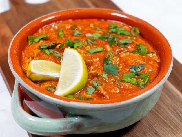 A bowl of rich and flavorful Sweet & Spicy Chili Chicken, garnished with fresh cilantro, green onions, and lemon wedges.