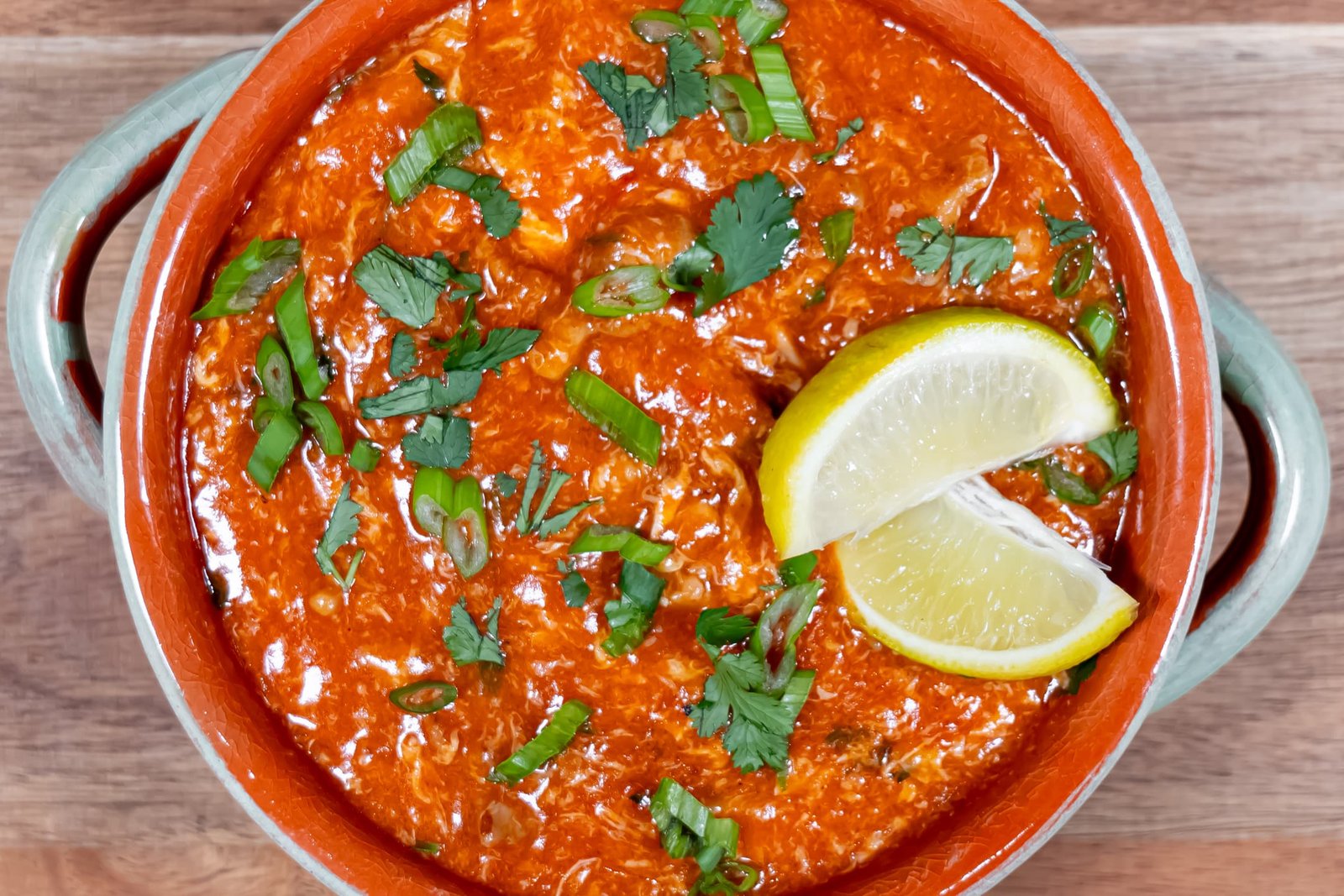 A close-up of Sweet & Spicy Chili Chicken, garnished with fresh cilantro, green onions, and lemon wedges, highlighting the rich, thick tomato-based sauce.