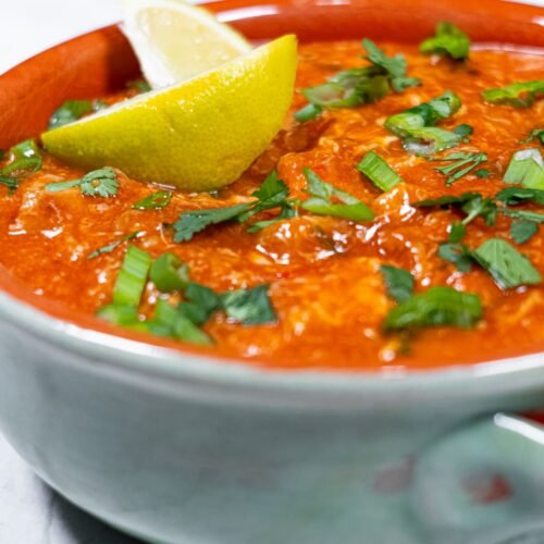 A bowl of sweet and spicy chili chicken garnished with fresh cilantro, green onions, and a lemon wedge.