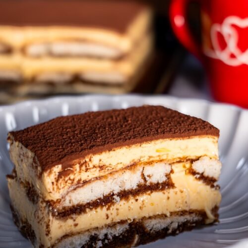 A slice of authentic Italian tiramisu with creamy mascarpone layers, soaked ladyfingers, and a dusting of cocoa powder, served on a white plate.