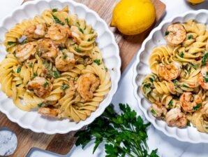 Mediterranean shrimp pasta with fusilloni, fresh parsley, and lemon in white bowls.