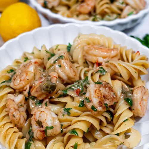 A bowl of Mediterranean shrimp pasta with fusilloni, garnished with fresh parsley, capers, and a light lemony sauce.